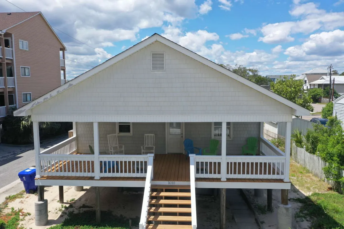 A large front porch featuring colorful chairs and steps leading up to the entrance. The space is open and welcoming, with a casual atmosphere perfect for relaxing, socializing, or enjoying a quiet moment with coffee. The porch's size and arrangement suggest there's enough room for pets to lounge or for a group to gather for meals or sunset drinks.