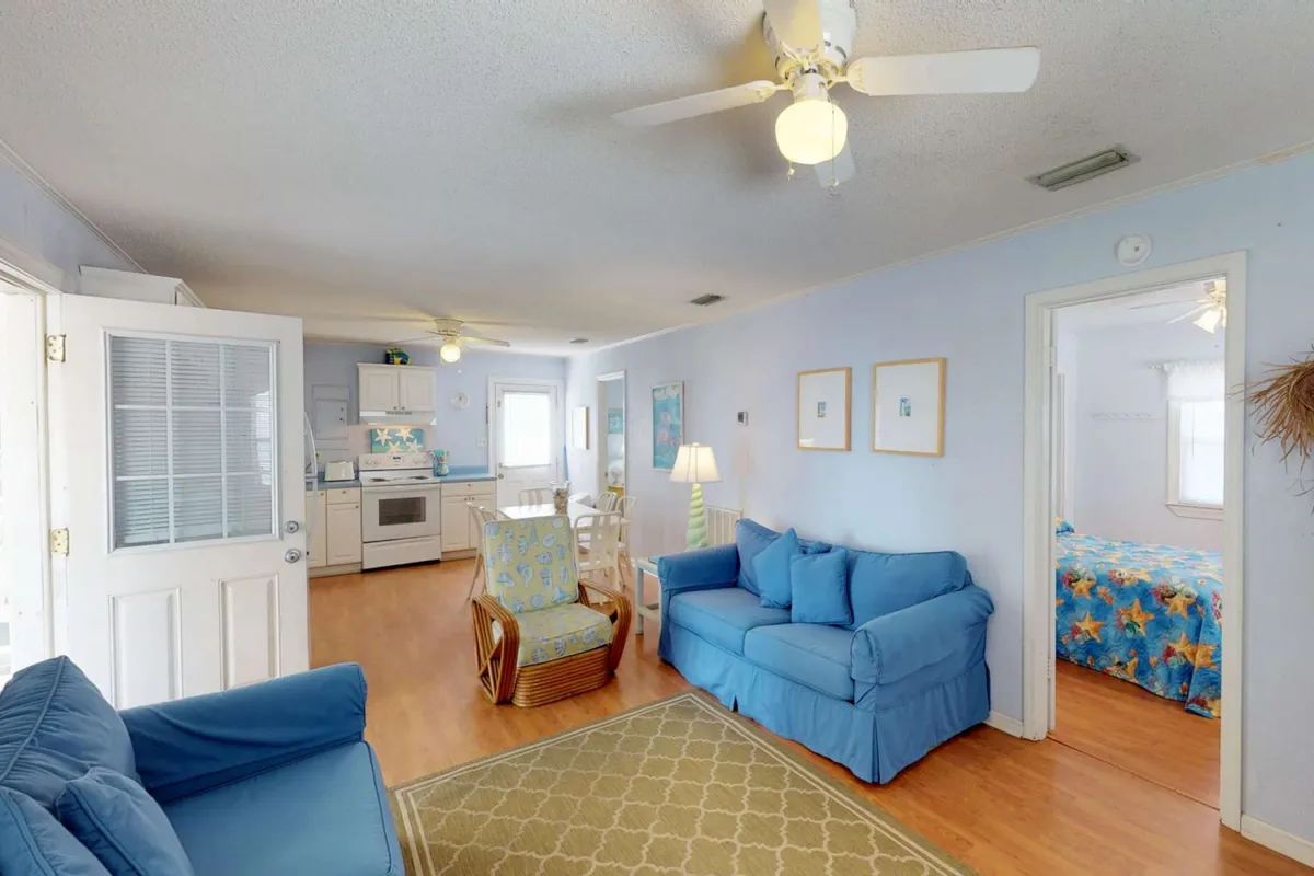 This image presents a spacious, open-concept living area where the kitchen seamlessly connects with the dining table and blue sofas. Decorative art adorns the walls, and the kitchen area includes visible appliances and ample counter space, highlighting the heart of communal activity in the home.