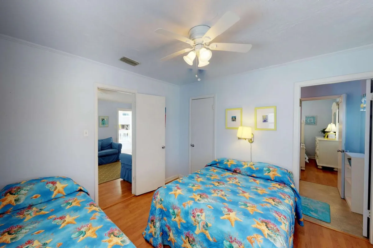 A comfortable bedroom with a colorful bedspread, ceiling fan, decorative wall art, and visible doorways. The room is designed for flexible use, with enough space for both fun sleepovers and quiet moments. The relaxed mood and layout suggest it can accommodate both a full and a twin bed, matching the description of Bedroom 2.