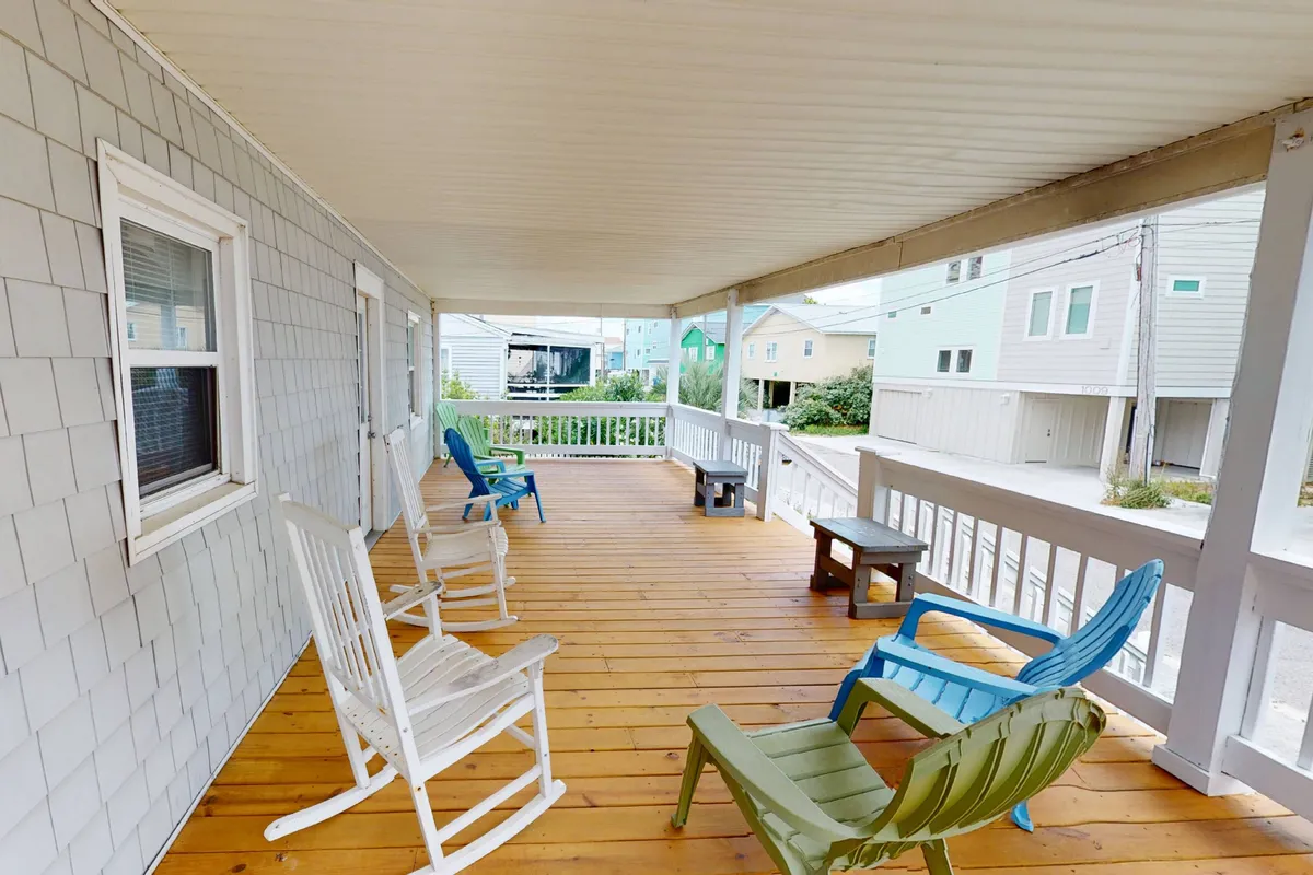 A wooden deck with colorful chairs and sturdy railings, arranged to encourage group gatherings and relaxation. The space looks perfect for family barbecues, casual outdoor meals, or simply lounging while enjoying the Carolina Beach breeze. There's ample space visible, which hints at pet-friendliness and the opportunity for alfresco dining at a picnic table or hosting friends.